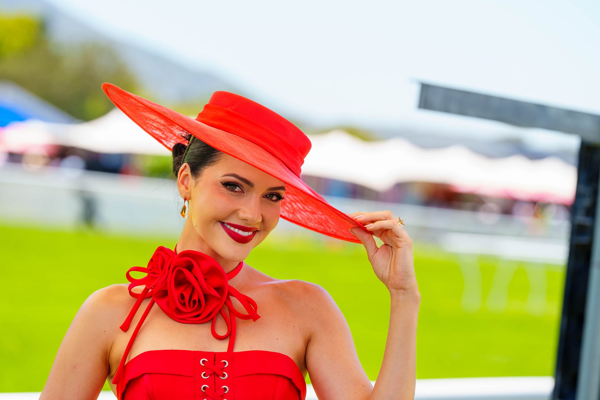 Cape Town MET lady in red holding the rim of her hat at the racecourse